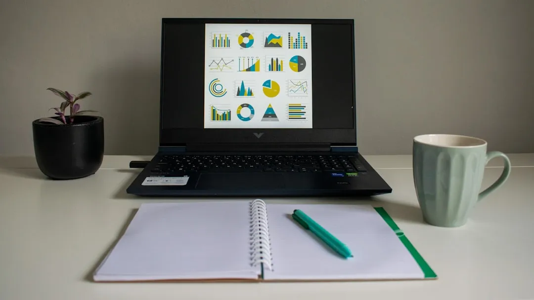 Laptop displaying financial charts next to notebook and mug on a professional desk