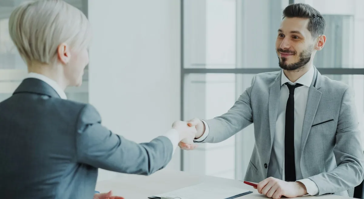 Two professionals shaking hands across a conference table during a business negotiation